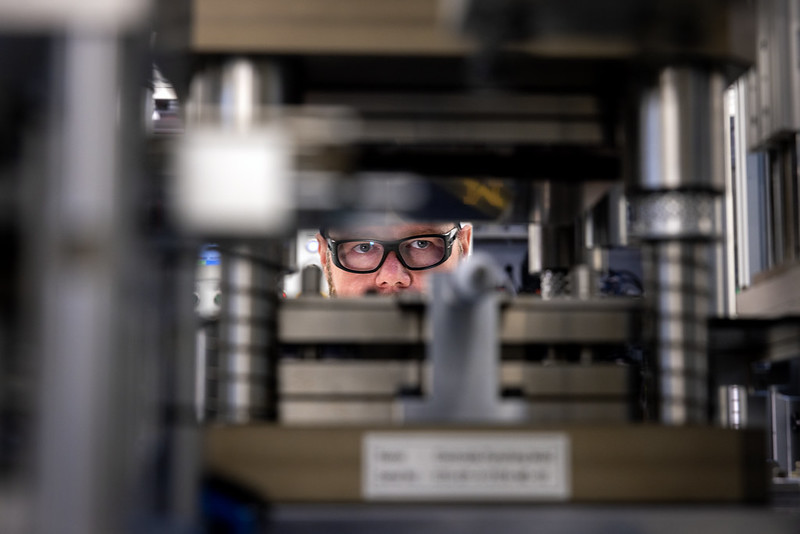 Man with safety goggles peering through battery making equipment