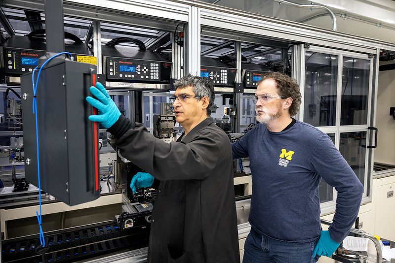 Two men operating battery making equipment